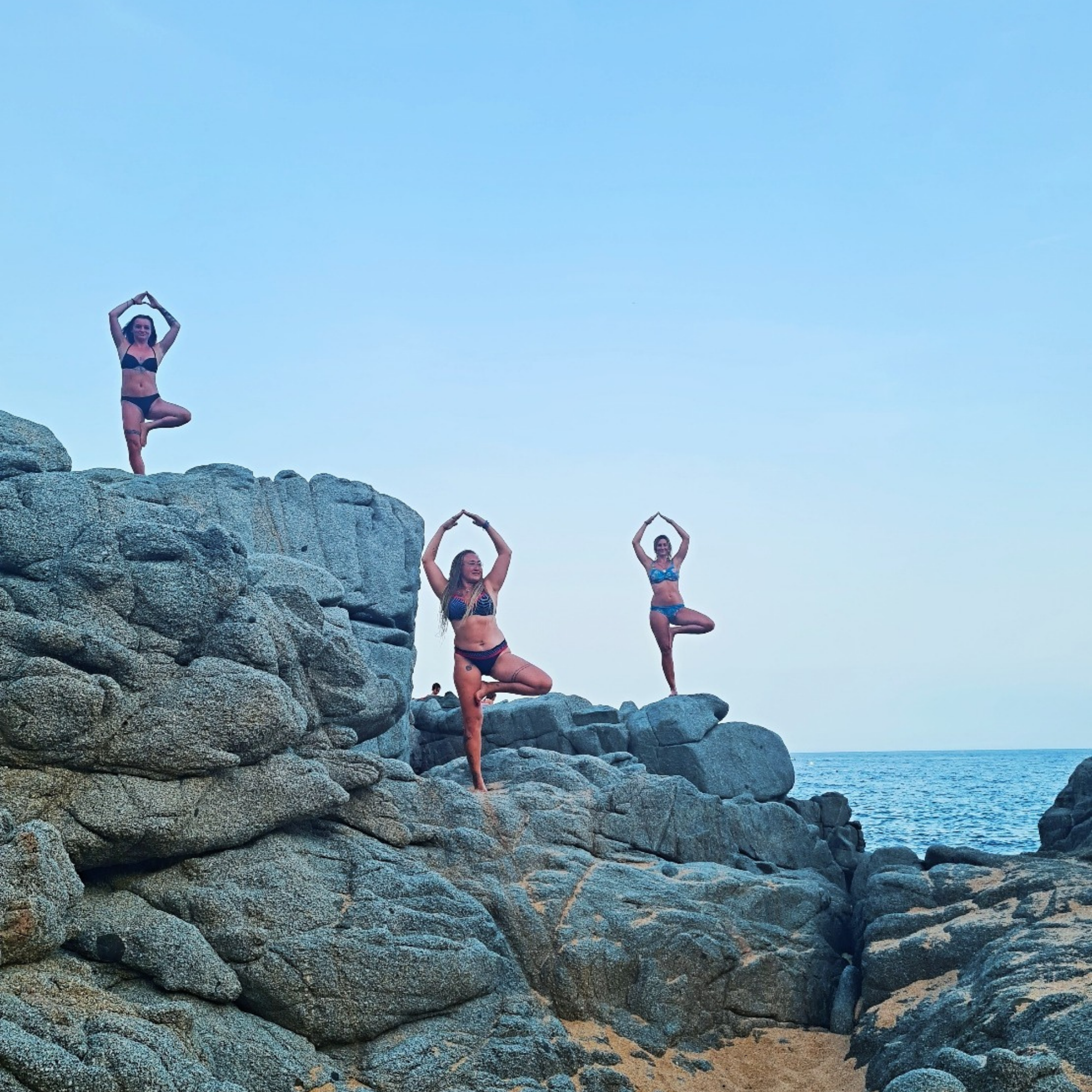 Eileen Kraus mit zwei Freundinnen in Baumposition auf Felsen am Meer